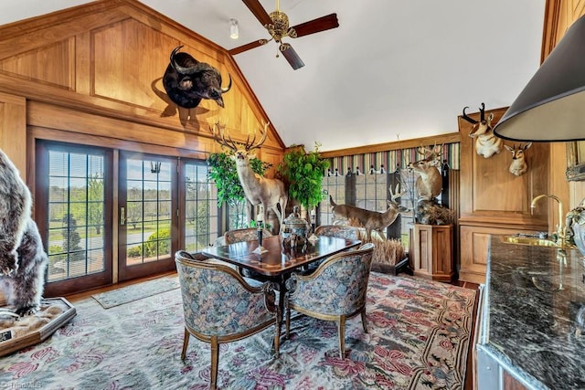 dining room featuring high vaulted ceiling, ceiling fan, hardwood / wood-style flooring, sink, and wood walls