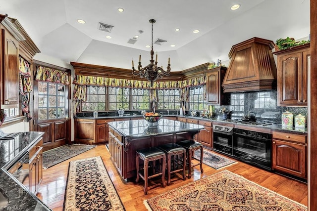 kitchen with light hardwood / wood-style floors, a kitchen island, black oven, vaulted ceiling, and decorative backsplash