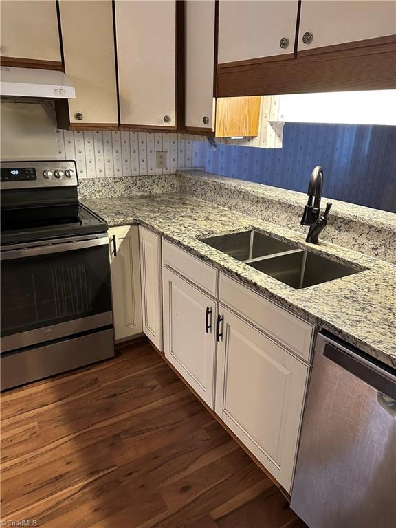 kitchen featuring dark wood-style flooring, a sink, under cabinet range hood, appliances with stainless steel finishes, and white cabinetry