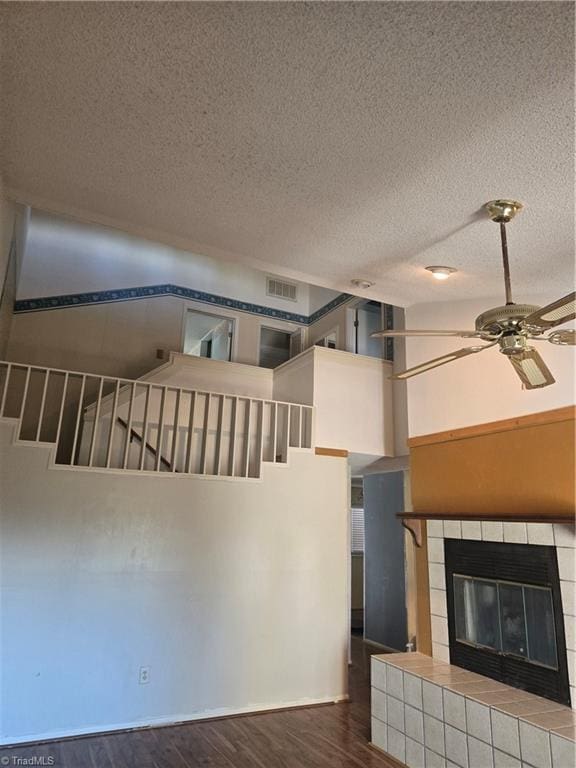 unfurnished living room featuring visible vents, a ceiling fan, wood finished floors, a high ceiling, and a fireplace