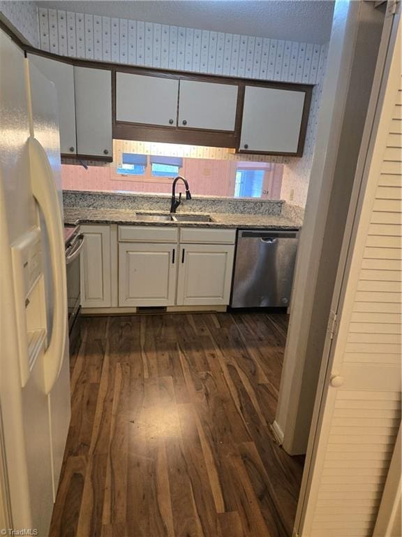 kitchen featuring a sink, stainless steel dishwasher, white refrigerator with ice dispenser, white cabinetry, and wallpapered walls