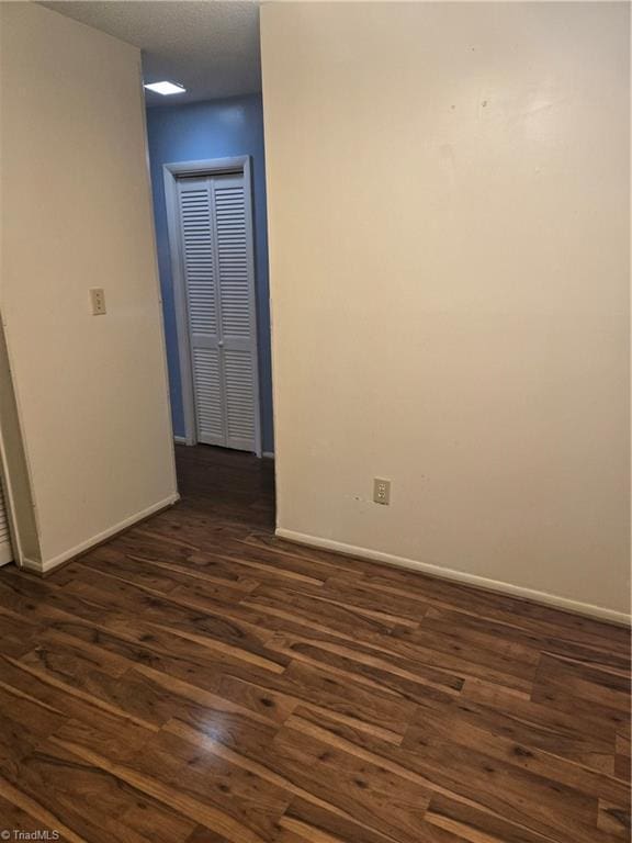 empty room featuring a textured ceiling, dark wood-type flooring, and baseboards