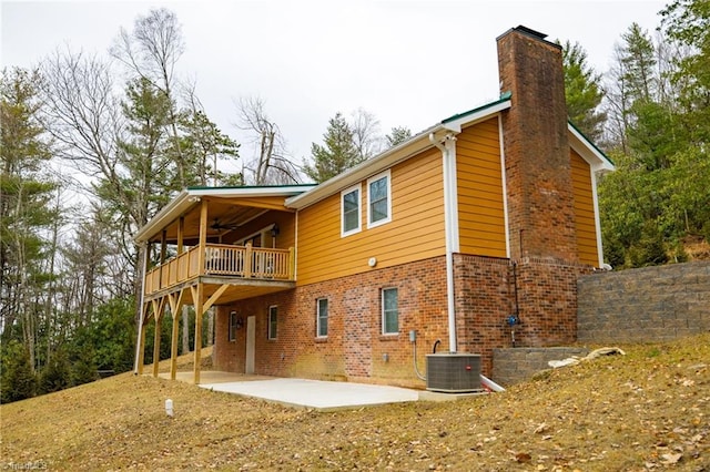 back of house with central air condition unit, brick siding, a ceiling fan, a chimney, and a patio area