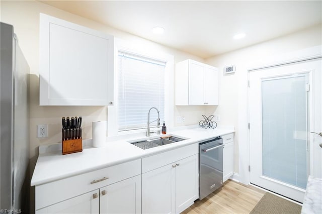 kitchen featuring white cabinets, stainless steel appliances, light countertops, light wood-type flooring, and a sink