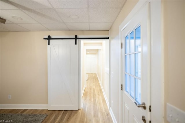 hall featuring light wood finished floors, a barn door, a paneled ceiling, and baseboards