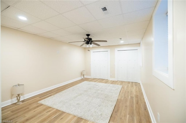 empty room featuring light wood finished floors, visible vents, a ceiling fan, a drop ceiling, and baseboards