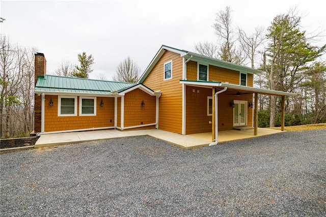 view of front of house with driveway, a patio, a chimney, metal roof, and french doors