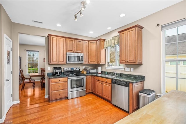 kitchen featuring dark stone counters, stainless steel appliances, light hardwood / wood-style floors, and sink