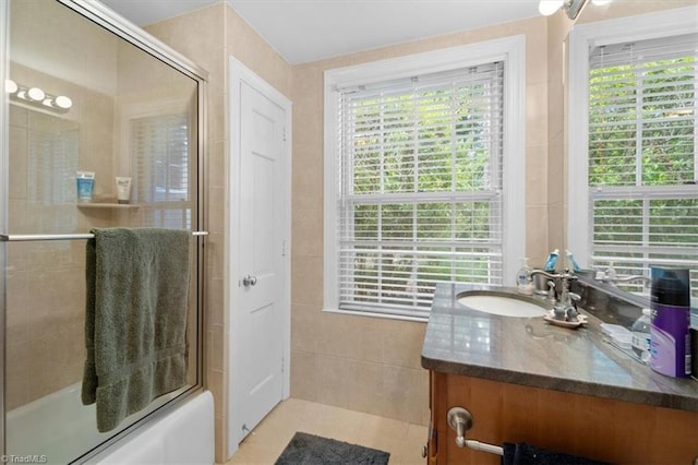 bathroom with vanity, combined bath / shower with glass door, a healthy amount of sunlight, and tile walls