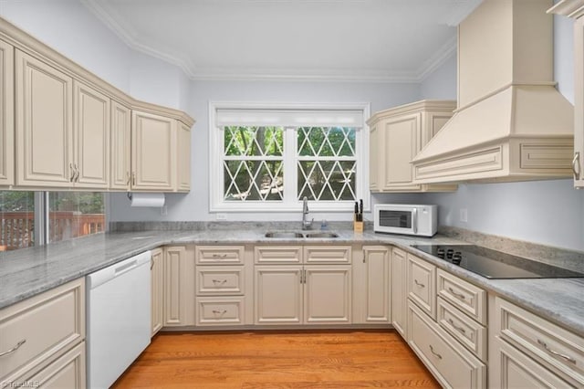 kitchen with premium range hood, light wood-style flooring, cream cabinetry, white appliances, and a sink