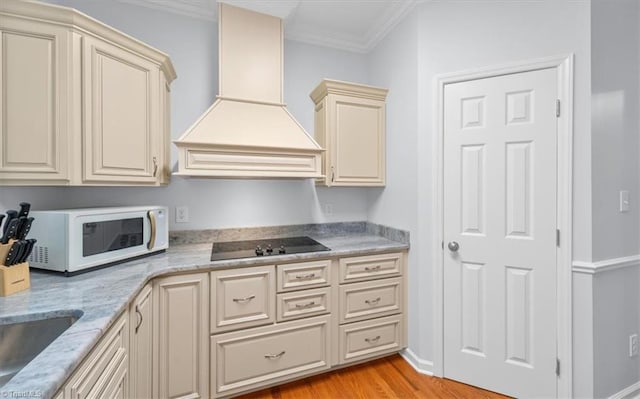 kitchen with white microwave, crown molding, black electric stovetop, cream cabinets, and custom exhaust hood