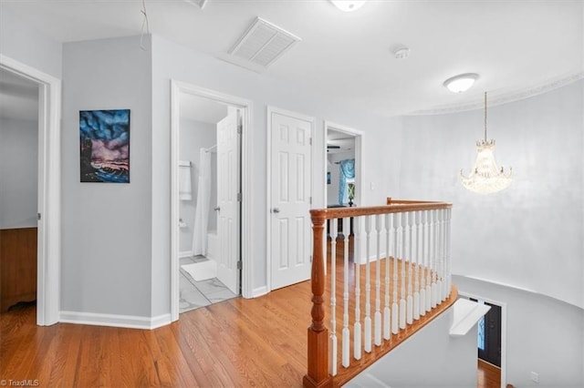 hall featuring visible vents, an upstairs landing, wood finished floors, an inviting chandelier, and baseboards