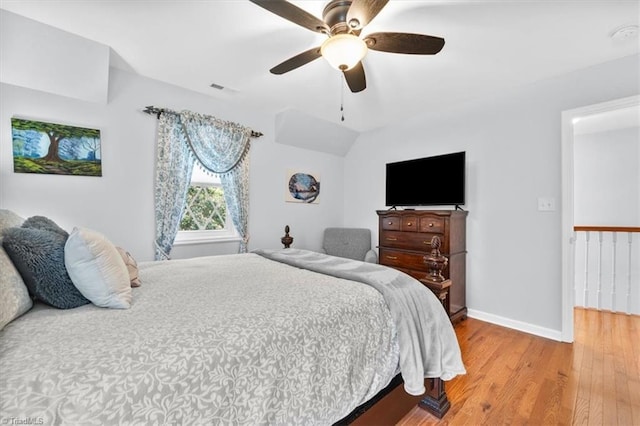 bedroom featuring light wood finished floors, visible vents, ceiling fan, baseboards, and vaulted ceiling