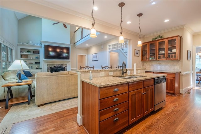 kitchen with a sink, light wood-style floors, stainless steel dishwasher, and light stone counters