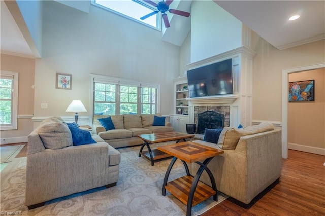 living room with wood finished floors, a stone fireplace, baseboards, high vaulted ceiling, and a skylight