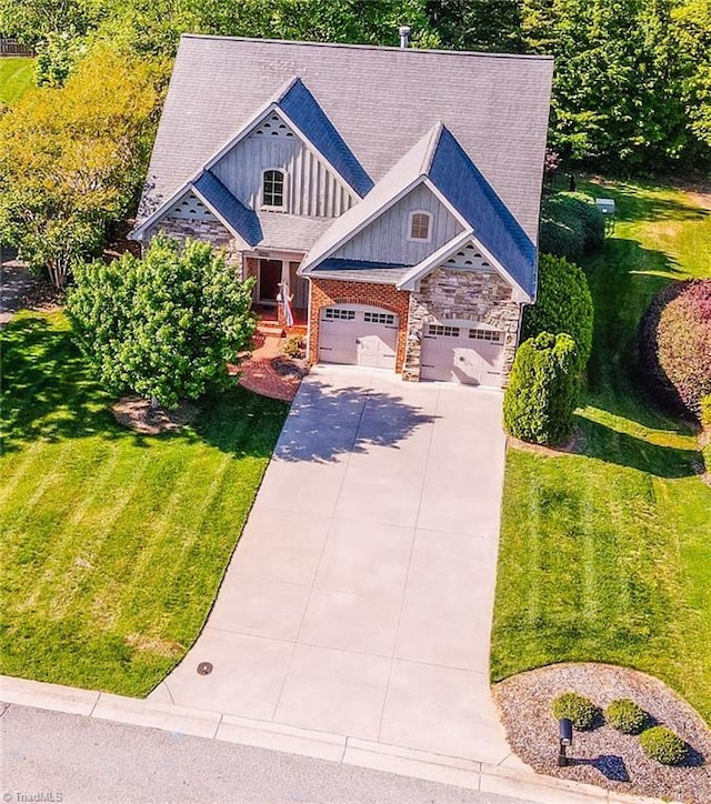 craftsman-style house with board and batten siding, a front lawn, concrete driveway, an attached garage, and stone siding