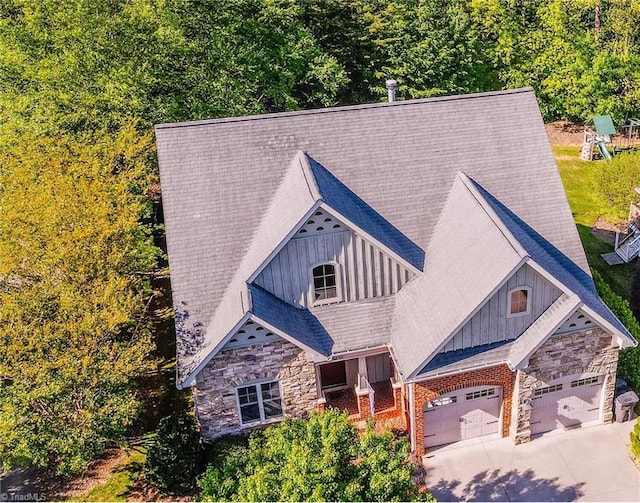 view of front facade with board and batten siding, an attached garage, concrete driveway, and stone siding