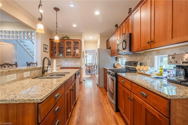 kitchen featuring brown cabinetry, light wood-type flooring, tasteful backsplash, a sink, and appliances with stainless steel finishes