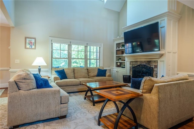 living room featuring baseboards, a stone fireplace, wood finished floors, and a towering ceiling