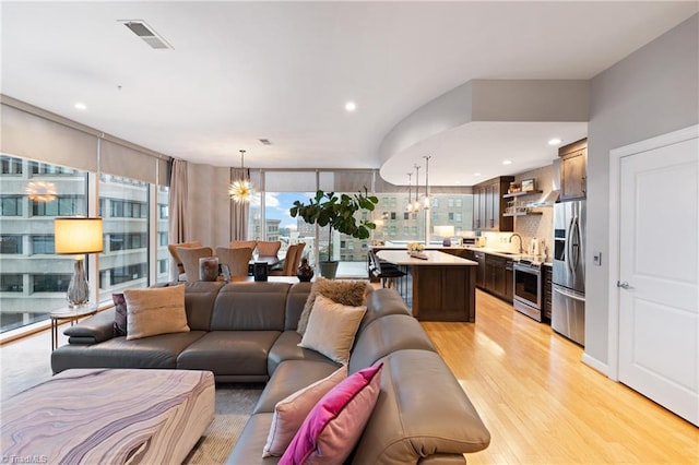 living room with light hardwood / wood-style flooring, a wall of windows, an inviting chandelier, and sink