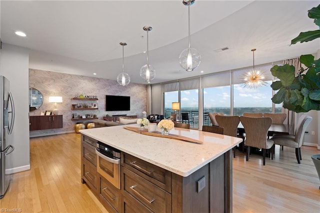 kitchen featuring a kitchen island, light stone countertops, light hardwood / wood-style flooring, decorative light fixtures, and stainless steel refrigerator with ice dispenser