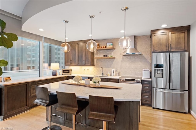 kitchen featuring tasteful backsplash, wall chimney exhaust hood, a kitchen island, stainless steel appliances, and light hardwood / wood-style flooring