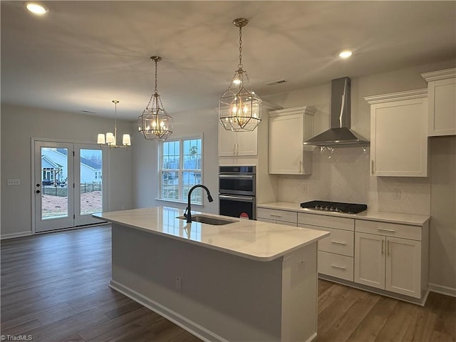 kitchen with appliances with stainless steel finishes, decorative light fixtures, an island with sink, sink, and wall chimney exhaust hood