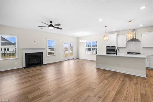 unfurnished living room featuring ceiling fan with notable chandelier, sink, and light hardwood / wood-style floors