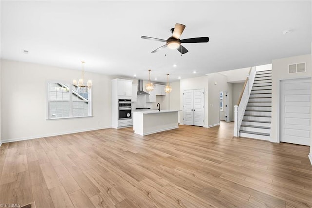 unfurnished living room with ceiling fan with notable chandelier, sink, and light wood-type flooring