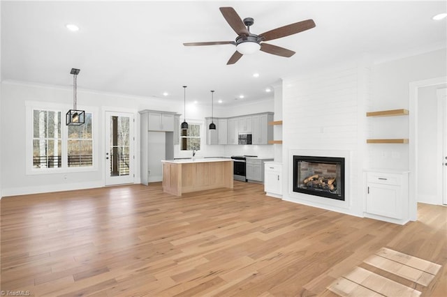 unfurnished living room featuring ornamental molding, a wealth of natural light, light wood-style floors, and a ceiling fan