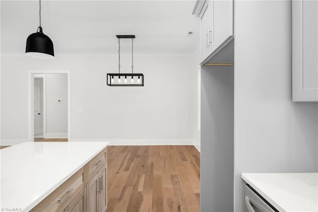 interior space featuring light countertops, ornamental molding, light wood-type flooring, and pendant lighting