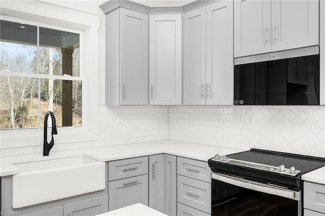 kitchen with light countertops, a sink, stainless steel range with electric stovetop, and decorative backsplash