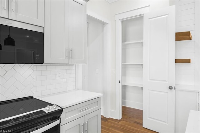 kitchen featuring light countertops, black range with electric cooktop, wood finished floors, and decorative backsplash