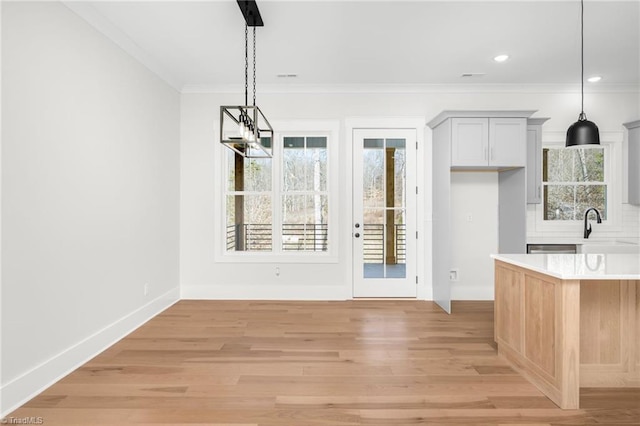 unfurnished dining area featuring baseboards, ornamental molding, light wood-style floors, a sink, and recessed lighting