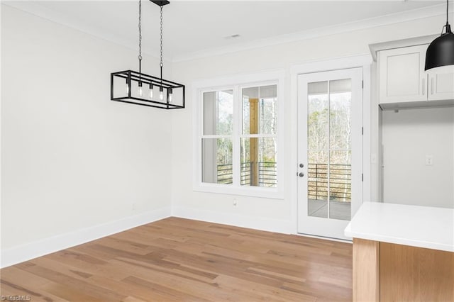 unfurnished dining area with light wood-style floors, crown molding, and baseboards