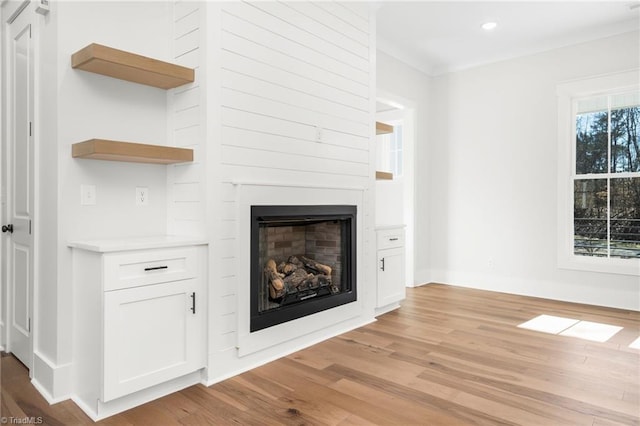 unfurnished living room featuring baseboards, a glass covered fireplace, crown molding, light wood-type flooring, and recessed lighting