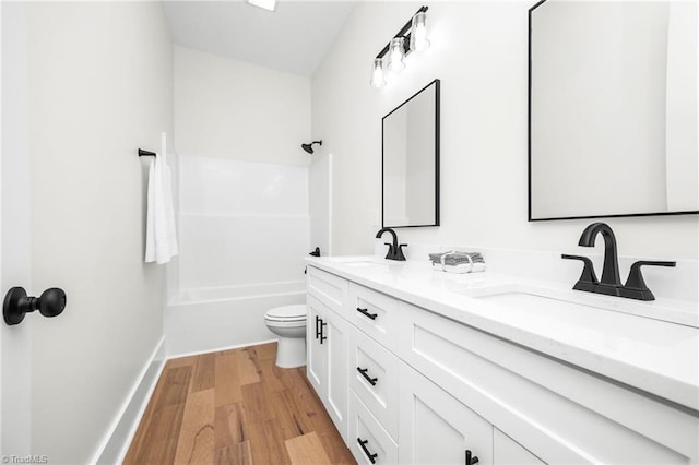 bathroom featuring double vanity, a sink, toilet, and wood finished floors