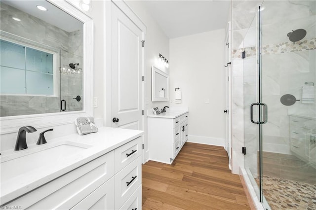 full bath with wood finished floors, two vanities, baseboards, a sink, and a shower stall