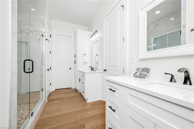 bathroom with a shower stall, two vanities, a sink, and wood finished floors