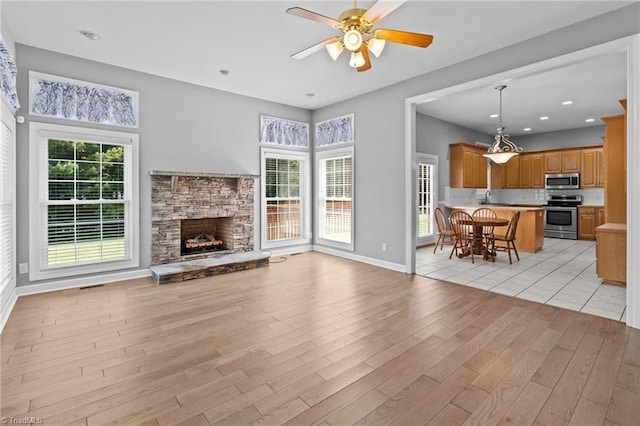 unfurnished living room featuring a fireplace, light hardwood / wood-style flooring, ceiling fan, and sink