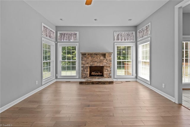 unfurnished living room with hardwood / wood-style floors, a stone fireplace, and ceiling fan