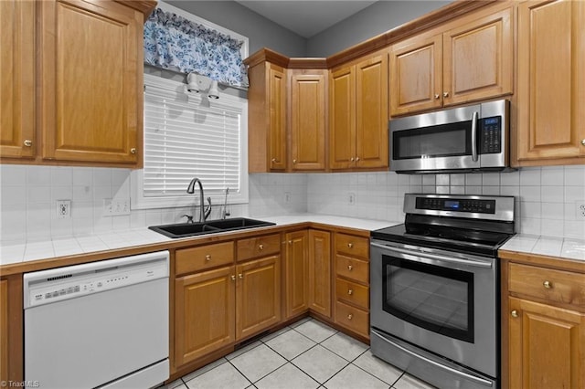 kitchen with tile counters, light tile patterned floors, sink, and appliances with stainless steel finishes