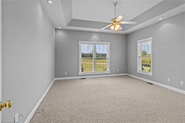 unfurnished room with a raised ceiling, ceiling fan, and carpet