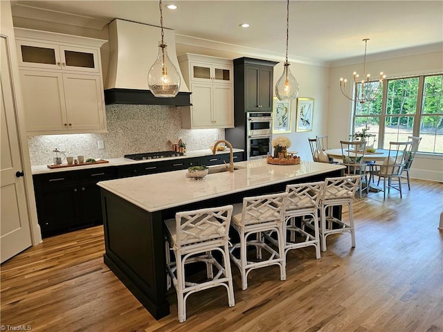 kitchen featuring white cabinetry, stainless steel appliances, crown molding, a center island with sink, and custom range hood