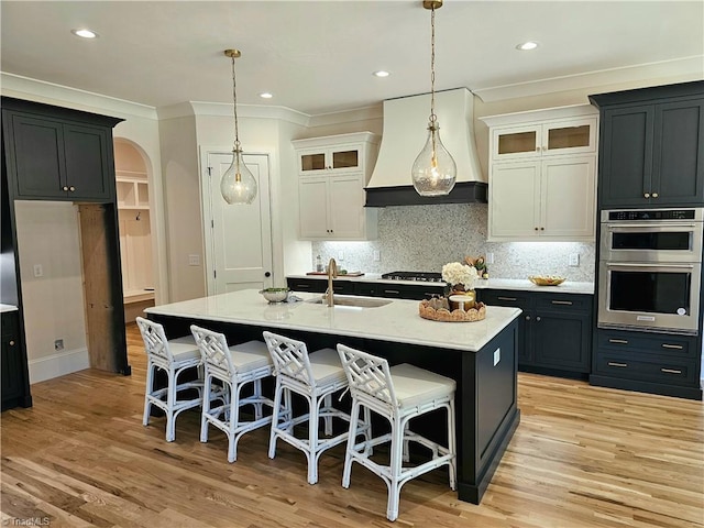 kitchen featuring sink, white cabinetry, custom range hood, and a kitchen island with sink