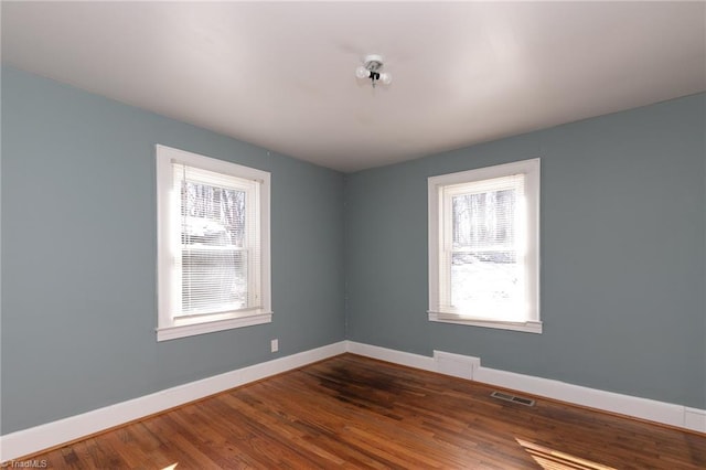 unfurnished room featuring wood finished floors, visible vents, and baseboards