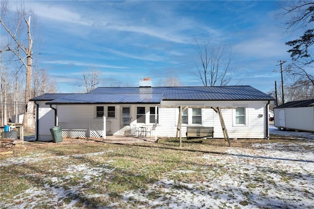 back of house featuring entry steps, metal roof, and a chimney