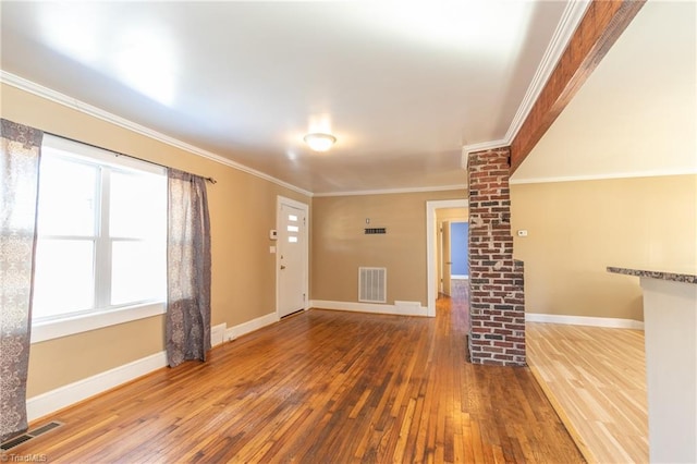 unfurnished living room with hardwood / wood-style flooring, baseboards, visible vents, and ornamental molding