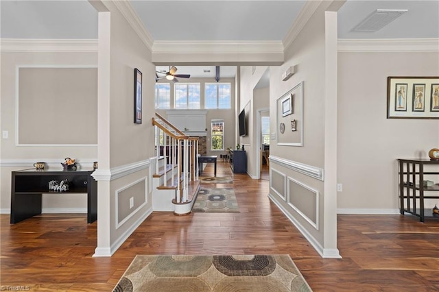 foyer featuring visible vents, stairway, wood finished floors, crown molding, and a decorative wall