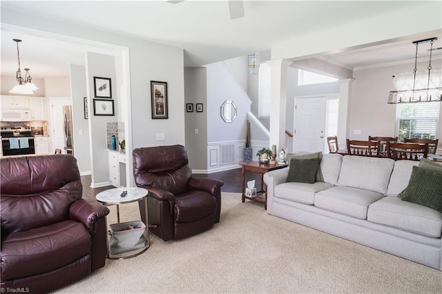 carpeted living area featuring a chandelier, stairway, ornamental molding, and ornate columns
